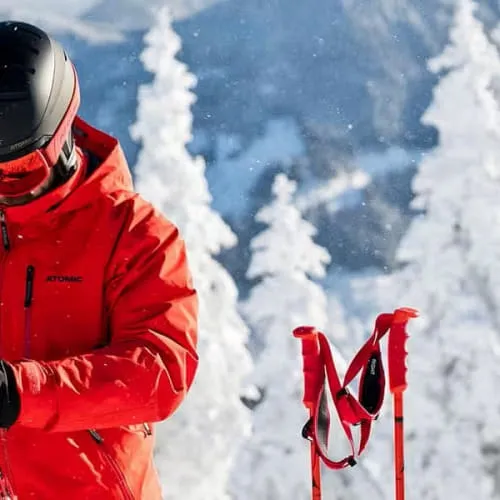 Skifahrer in roter Jacke mit Ski in verschneiter Landschaft